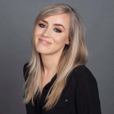 A person with long, blonde hair wearing a black shirt smiles softly against a gray backdrop, capturing a perfect moment of event photography.